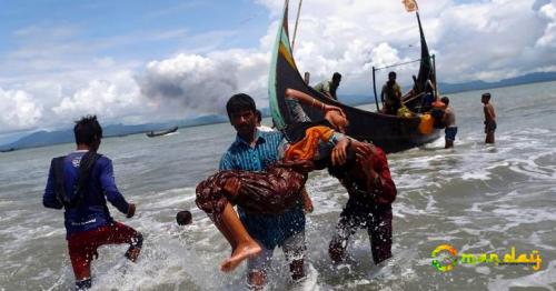 Smoke is seen on Myanmar&rsquo;s side of border as an exhausted Rohingya refugee woman is carried to the shore after crossing the Bangladesh-Myanmar border by boat through the Bay of Bengal