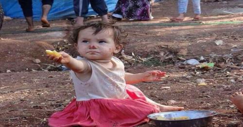 Refugee toddler offers food to a journalist who came to take a picture of her